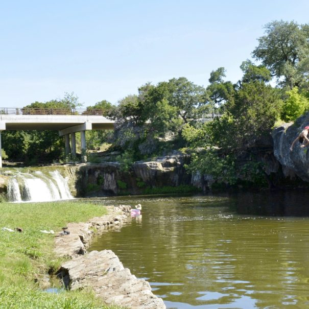 Two boys jumping from rock into pond